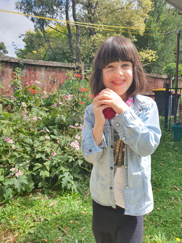 A 6 year old girl standing in a garden smiling and squeezing a red balloon EcoSplat reusable water balloon between her hands.