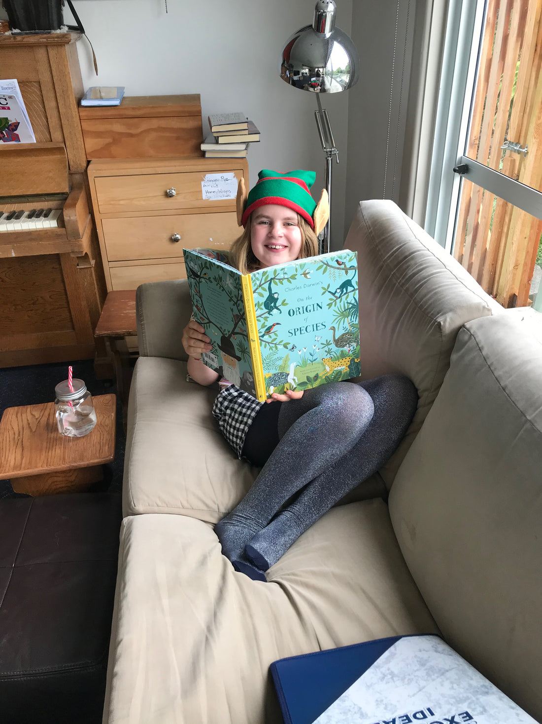 A 11 year old girl wearing a Christmas hat sitting on a sofa reading a book