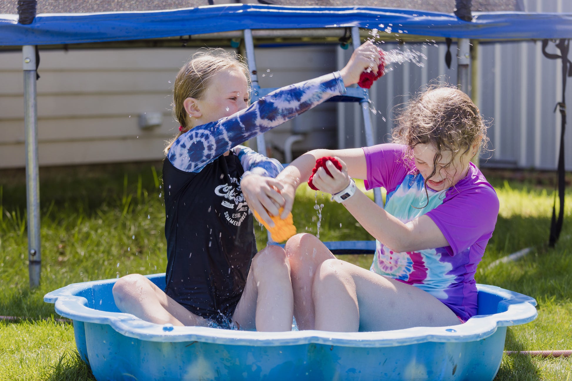Two girls laughing and sitting in a paddling pool and playing with EcoSplat Reusable Water Balloons