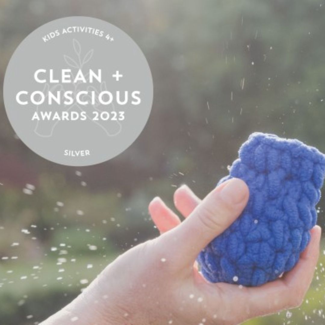 A blue Ecosplat Reusable Water Balloon held in a hand, splashes of water coming off it. With a logo Clean + Conscious Awards 2023, Silver, Kids Activities 4+